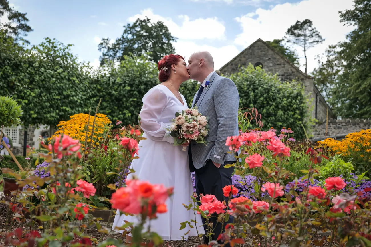 Newlyweds kissing among colourful garden flowers